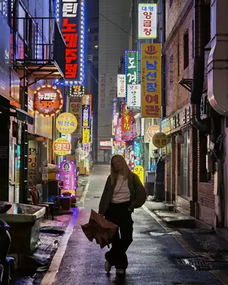 Eu numa rua de letreiros neon em Busan, à noite